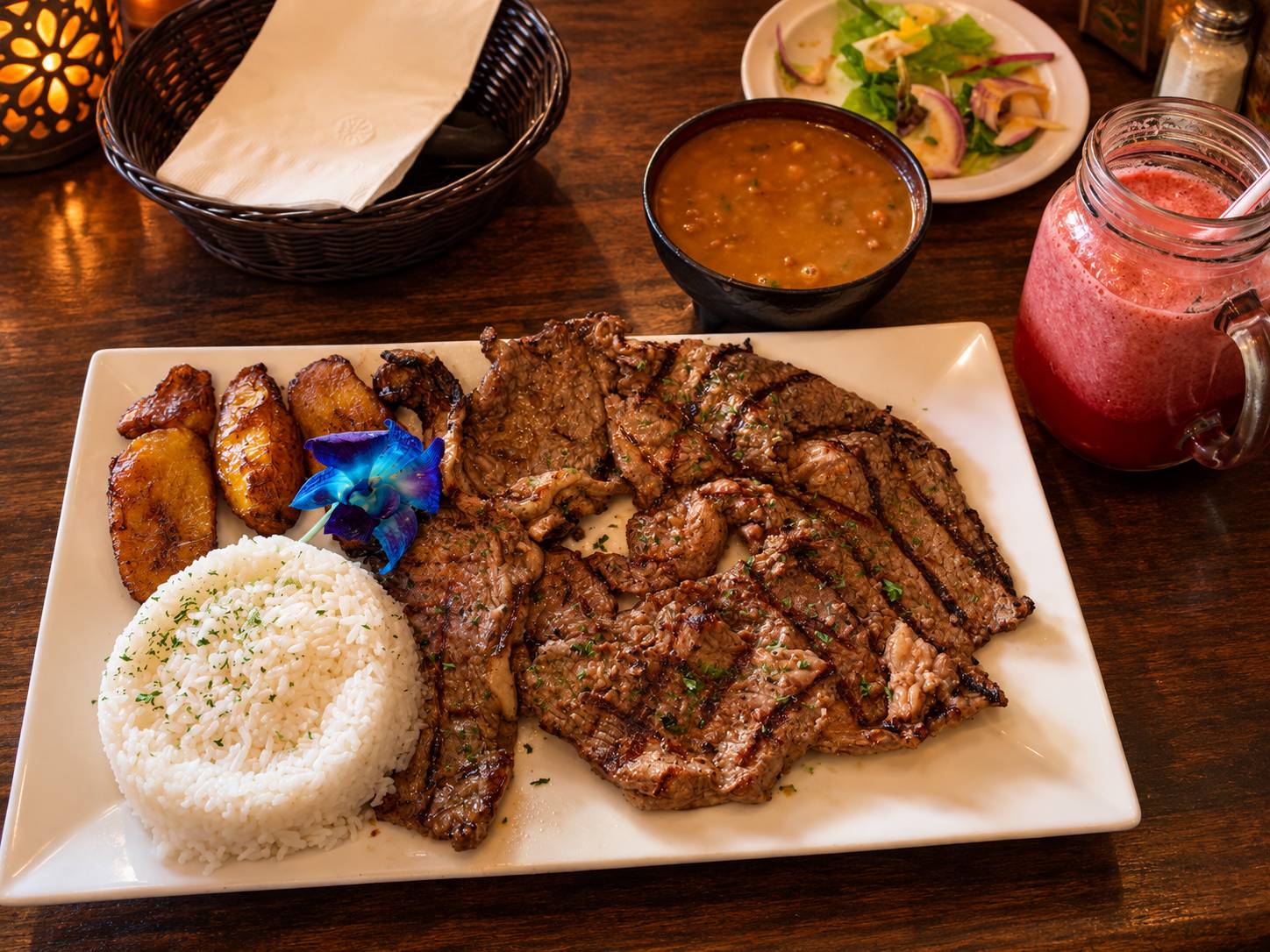 Grilled beef slices with white rice, fried sweet plantains and a side of beans.