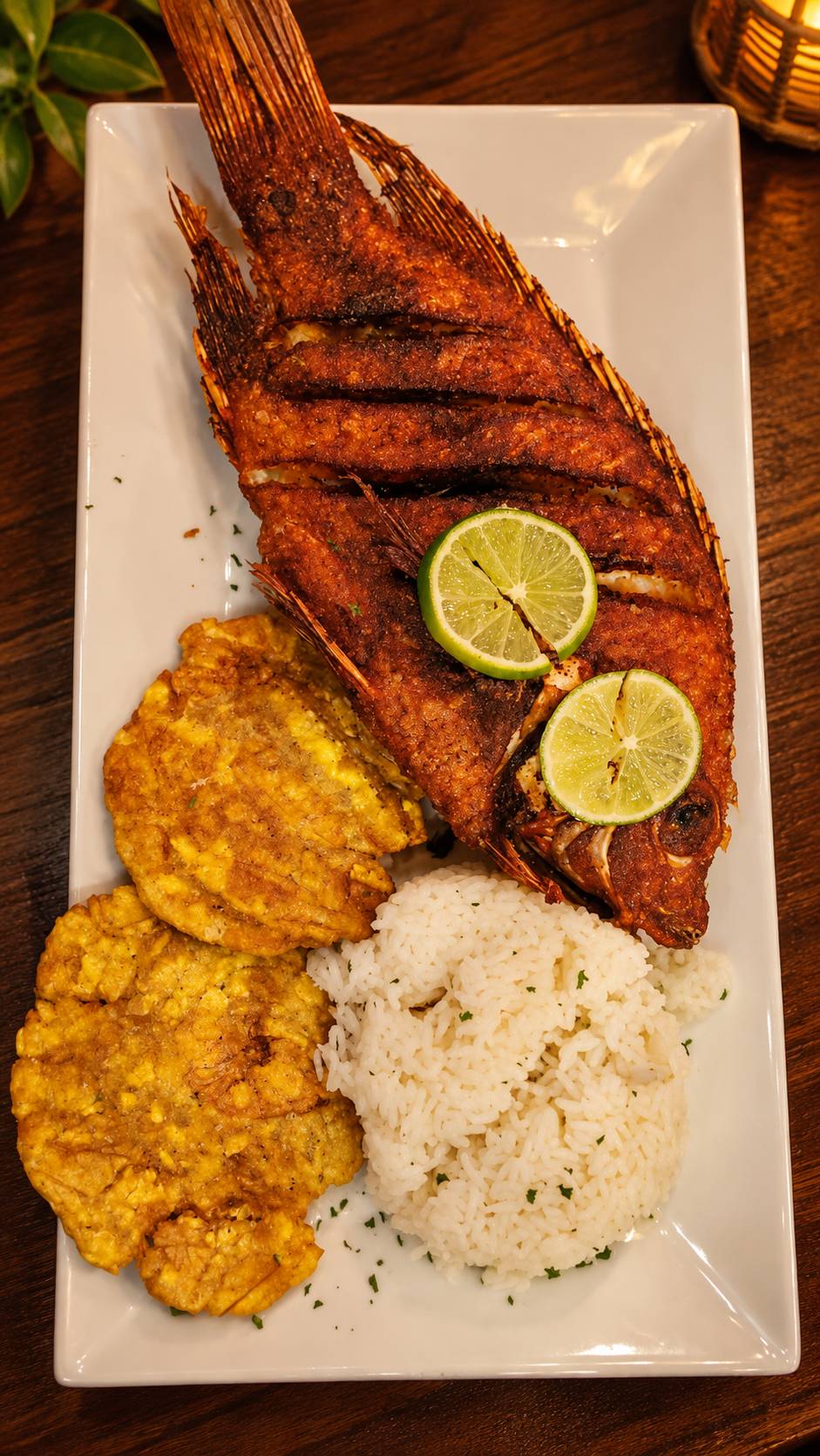 Whole fried fish with lime slices, fried green plantains and white rice.