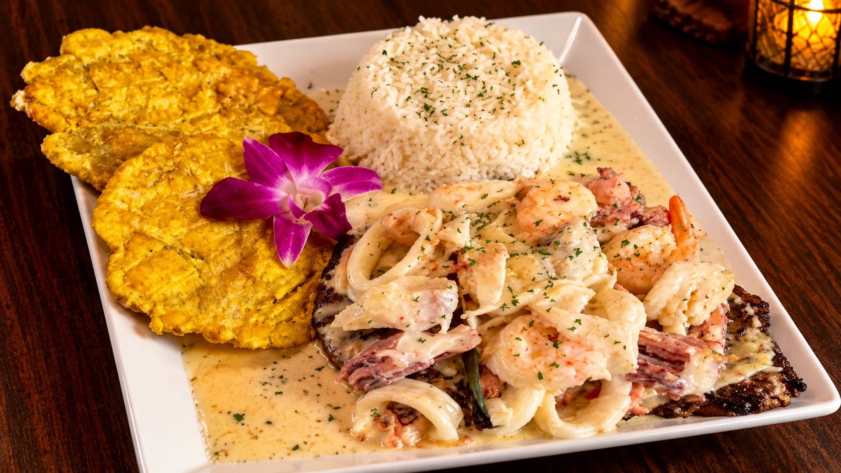 Grilled plate topped with shrimp, calamari and seafood cream sauce, with white rice and fried green plantains.